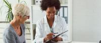 A doctor smiling and talking to their patient while writing something on their clipboard
